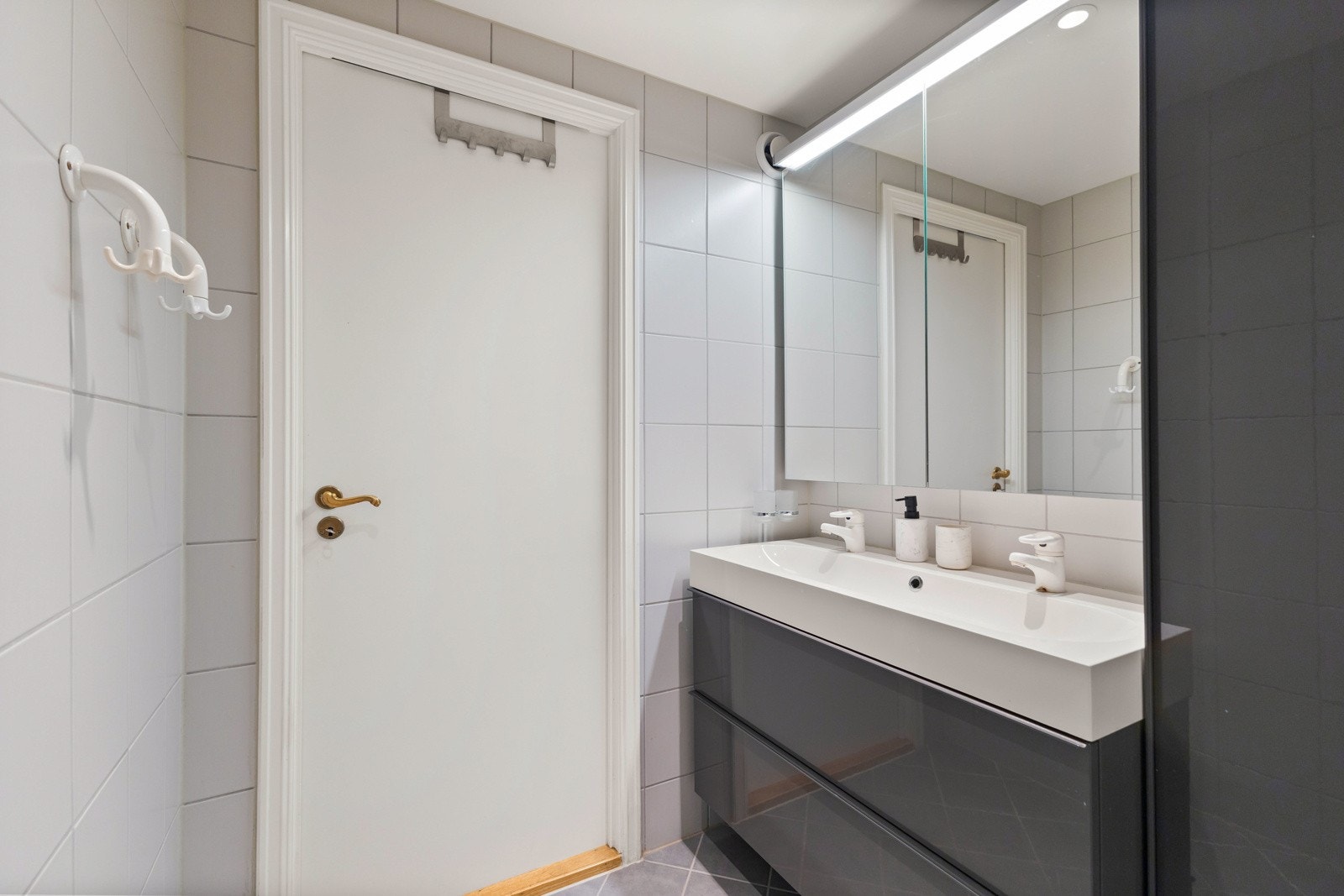 Badet inneholder mørk innredning i form av høyskap og underskuffer med servant samt speilskap over. Det er videre boblebad med støpsel for tilkobling, badekaret har dusjarmatur Galleribilde