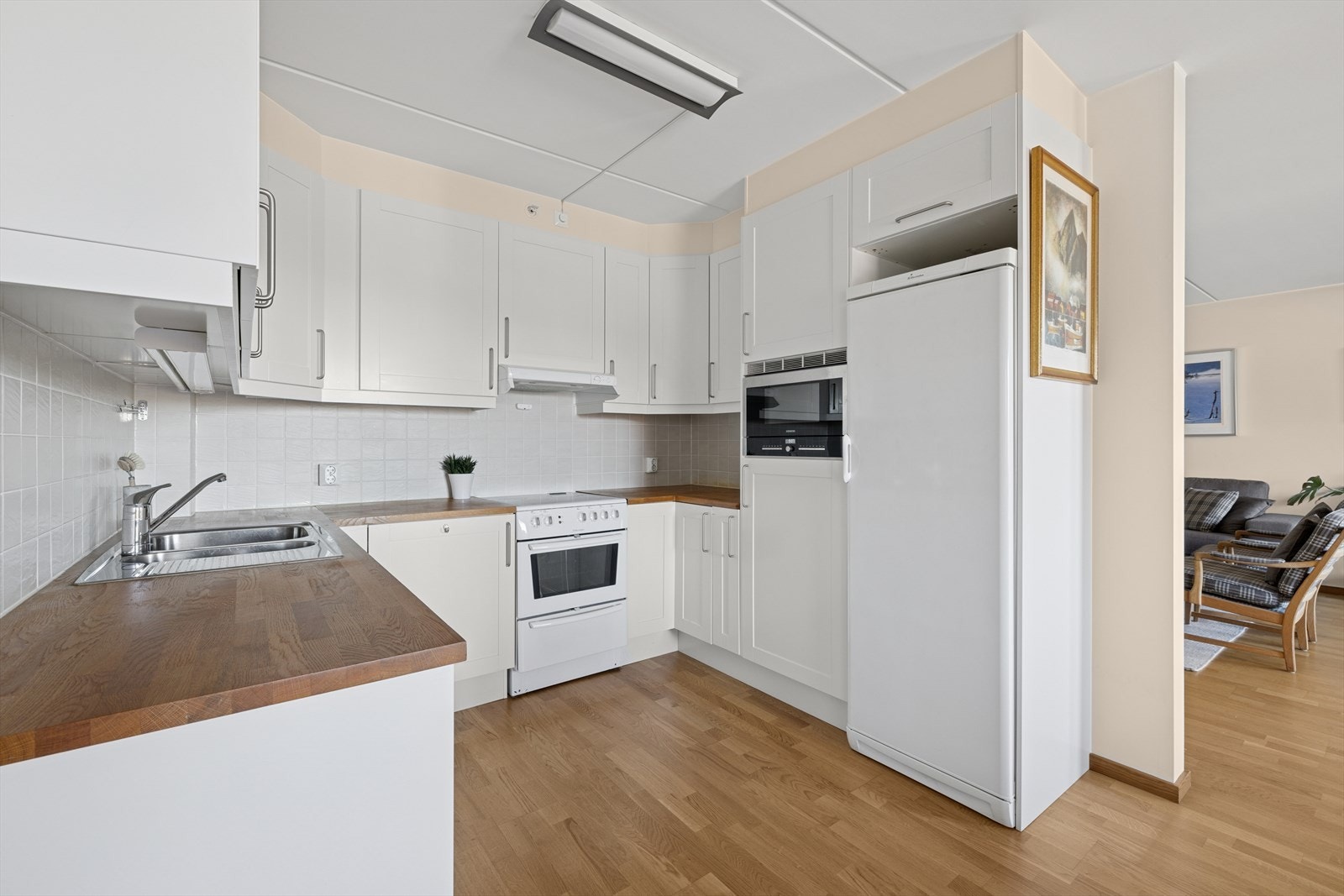 Kjøkkenet har innredning med profilerte fronter. Heltre benkeplate med nedfelt kum i rustfritt stål. Lys under overskap. Fliser på vegg over benk. Galleribilde