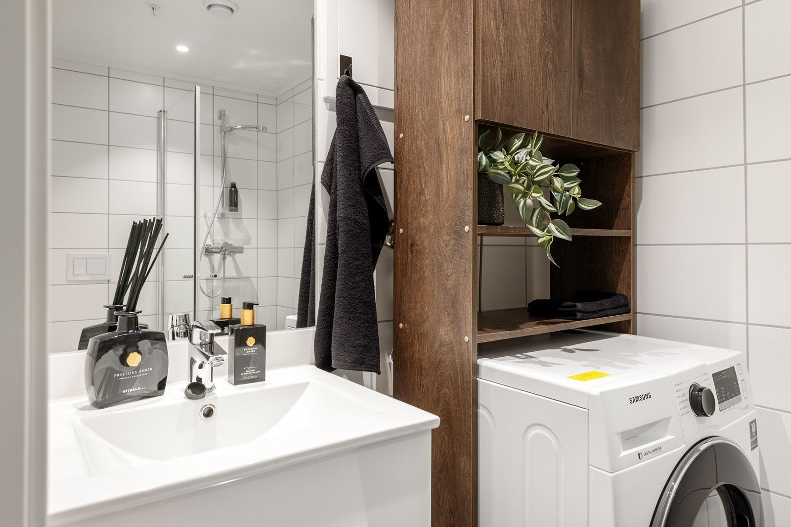 Baderommet er innredet med servant med underskap, speil med tilhørende belysning, dusj, veggmontert wc og opplegg for vaskemaskin Galleribilde