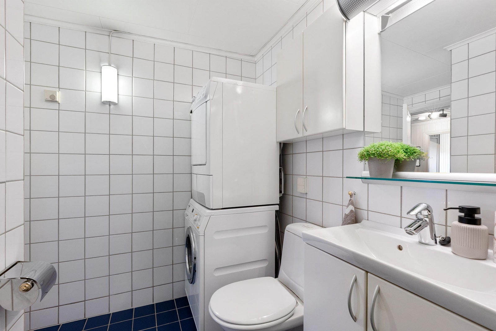 Badet har toalett, vegghengt servantinnredning med ovenpåliggende servant, speil med overlys over servant, dusjkabinett og opplegg for vaskemaskin Galleribilde