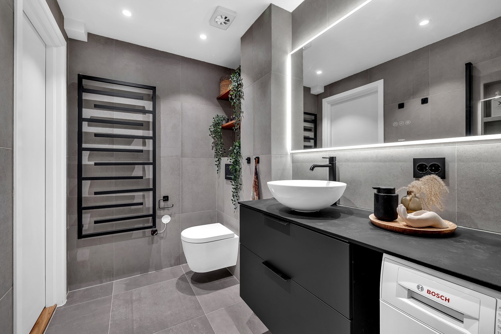 Badet har dusjhjørne med regnfallsdusj, servant med underskap og opplegg for vaskemaskin, vegghengt wc, speil og hånkletørker. Galleribilde