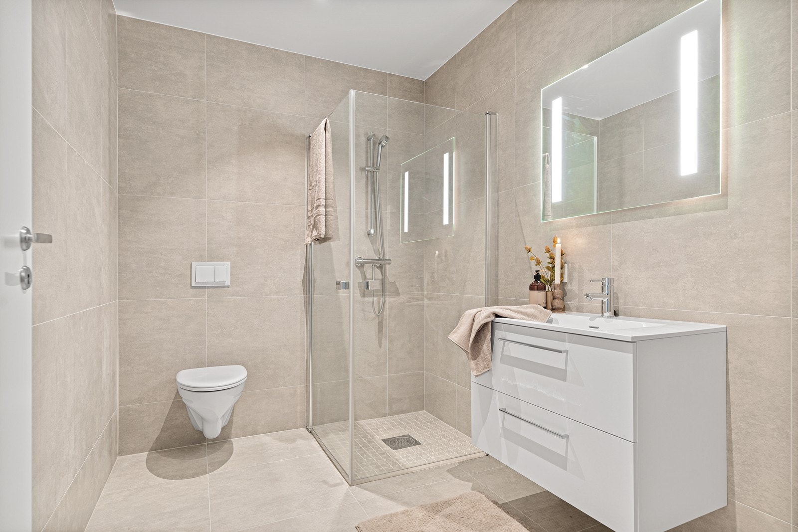 Lekkert flislagt bad med nedfelt servant, vegghengt toalett og dusjhjørne med innfellbare dører Galleribilde