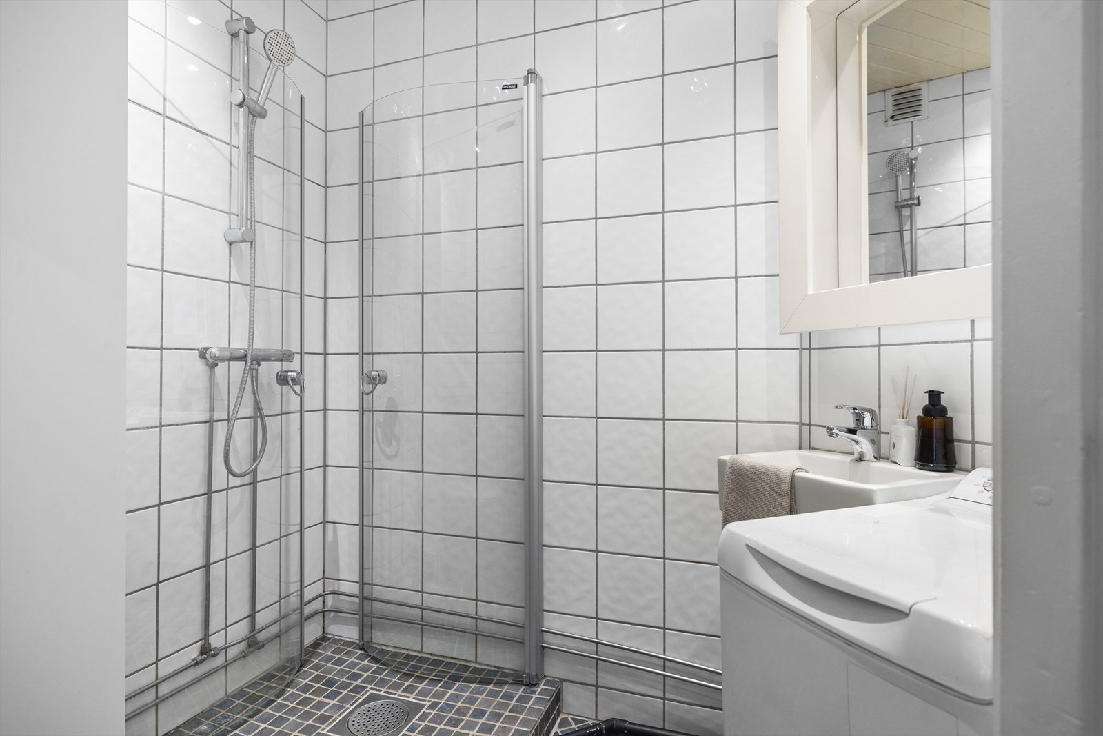 Badet har flislagte vegger og gulv med fliser på betong, samt malt panel i himlingen. Dusjsonen er hevet og avskjermet med dører i herdet glass. Rommet er innredet med benkeskap med glatte fronter og servant i helstøpt plate. Opplegg for vaskemaskin Galleribilde