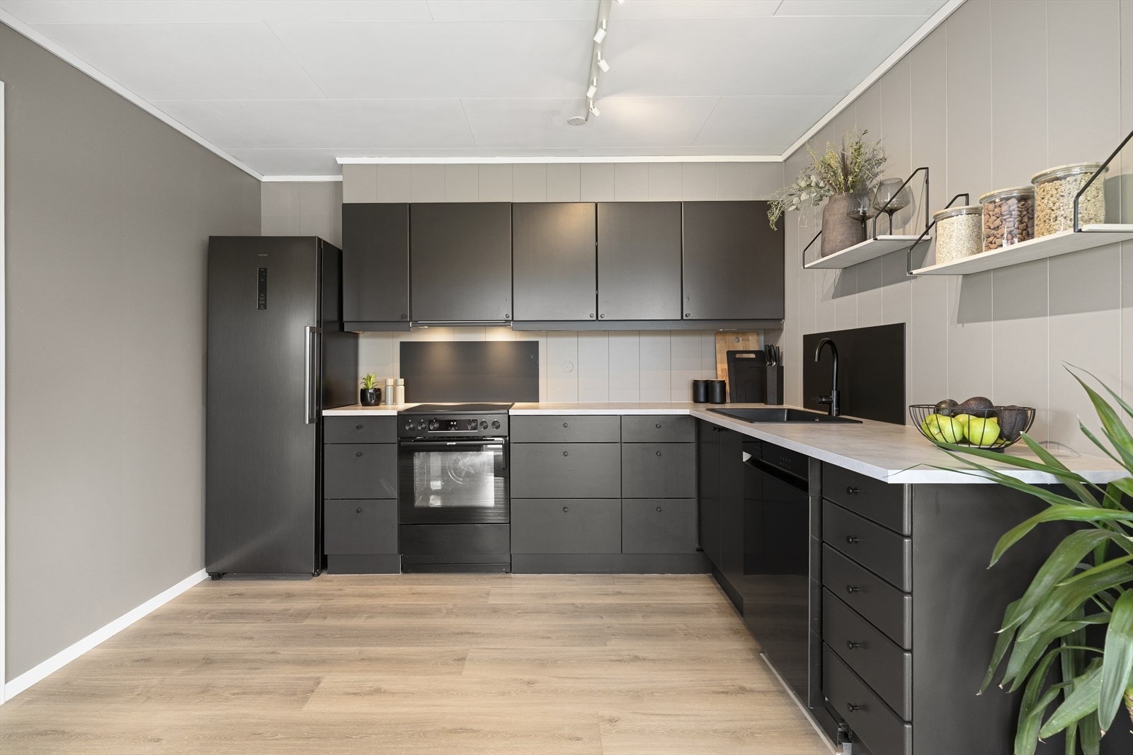 Kjøkkeninnredning med sorte, glatte fronter og benkeplate av laminat. Kjøkkenet har godt med skap- og benkeplass, samt frittstående hvitevarer som medfølger i handelen. Galleribilde