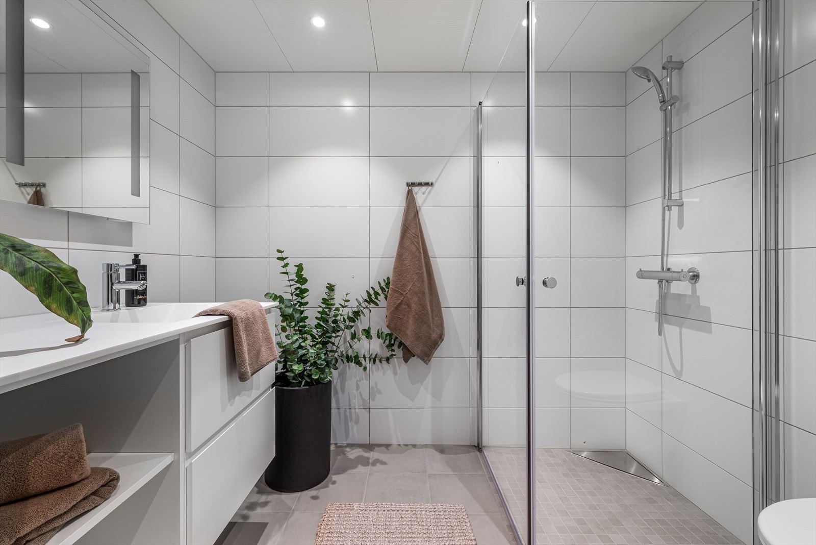 Badet har fliser på gulv, lekker baderomsinnredning med hvite profilerte fronter, vegghengt wc og opplegg for vaskemaskin. Galleribilde