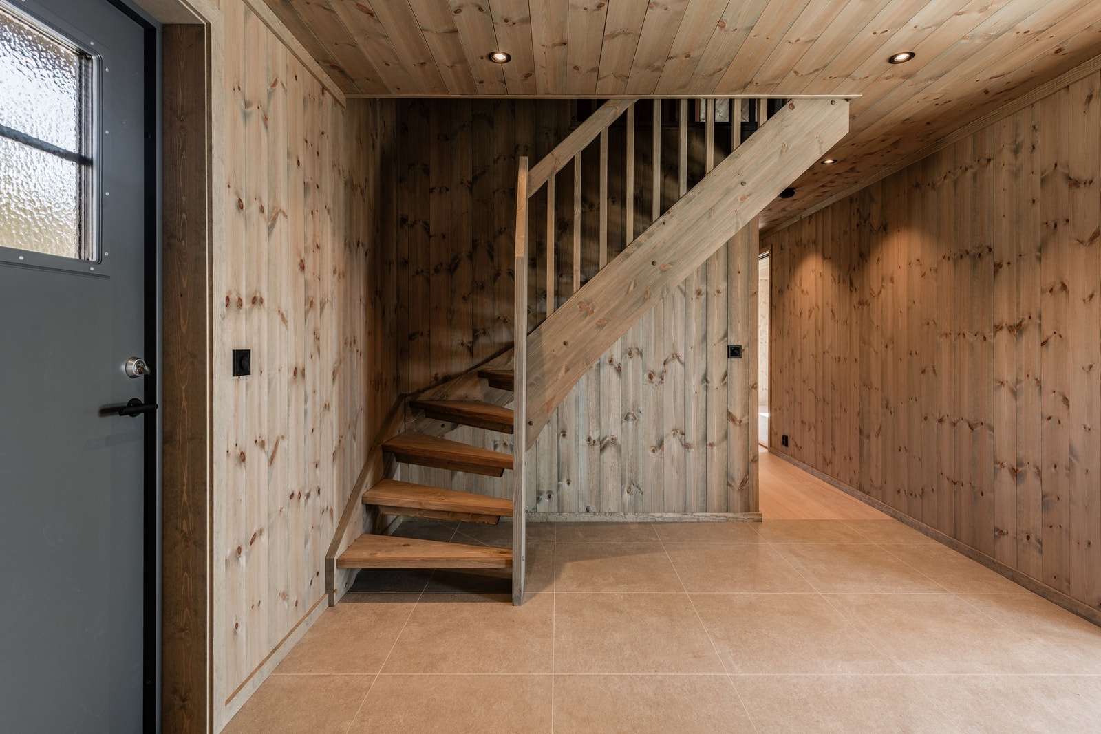 Åpen beiset furutrapp med spile rekkverk i tre går opp til hyttens andre etasje Galleribilde