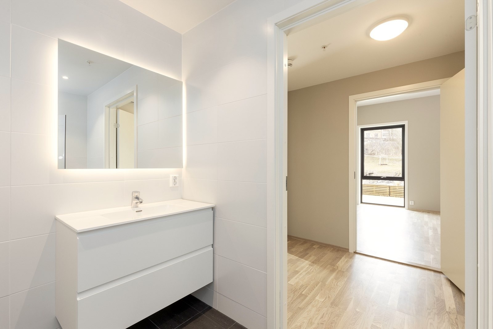 Bad har dusjnisje med glassdører, vegghengt toalett og innredning med vask og speil med lys. Galleribilde