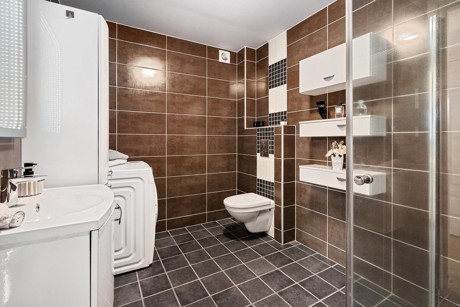 Badet i utleieleilighet i 1. etg. har nedfelt servant skuffer med glatte fronter. Det er høyskap og dusjhjørne og opplegg for vaskemaskin. Galleribilde