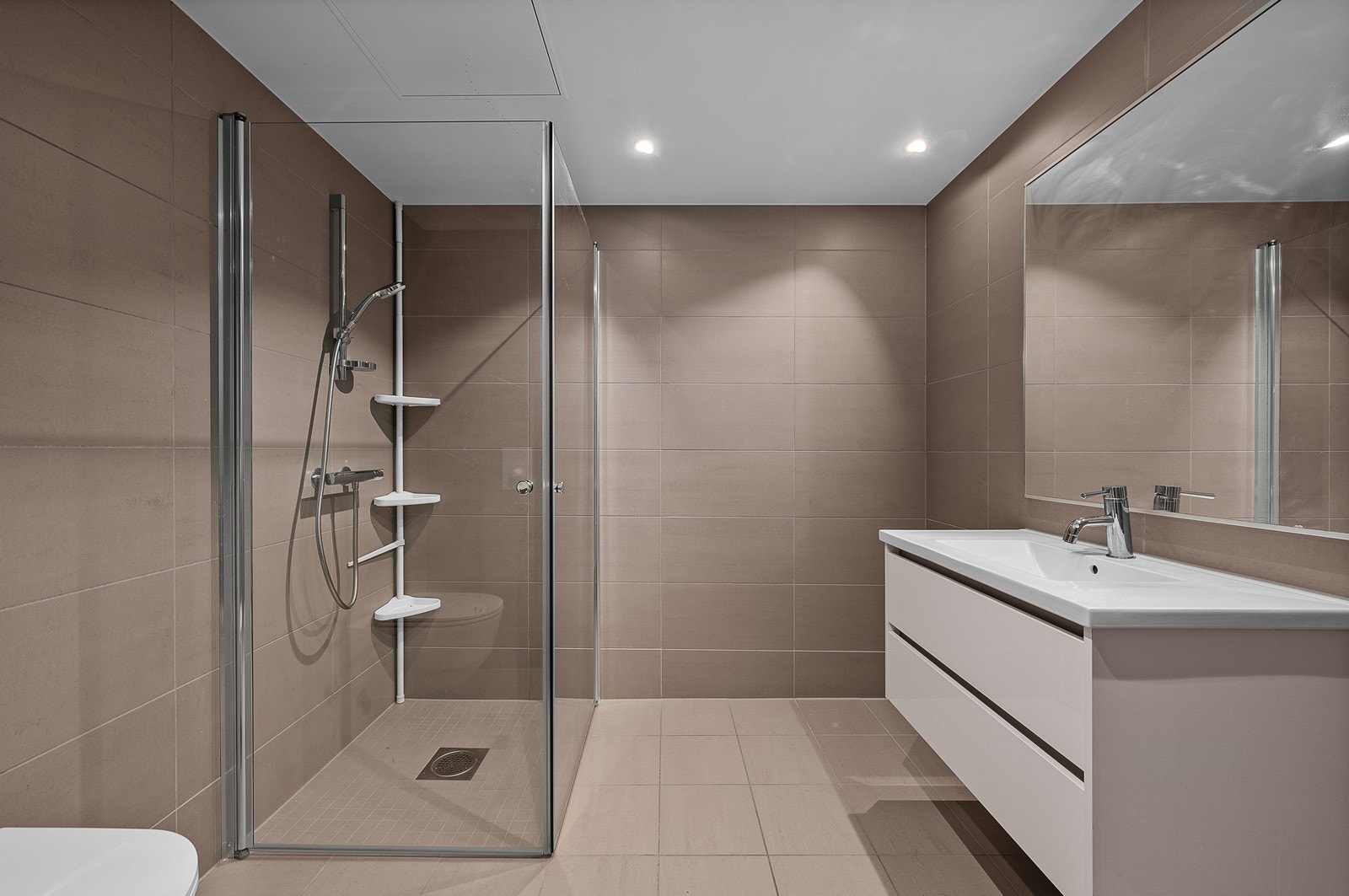 Moderne flislagt bad med varme i gulv og downlights i himling Galleribilde