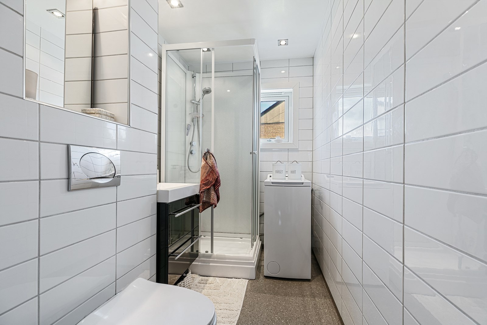 Baderom med flislagte vegger og belegg på gulv. Badet er utstyrt med vegghengt toalett, servant med skuffer og dusjkabinett. Galleribilde