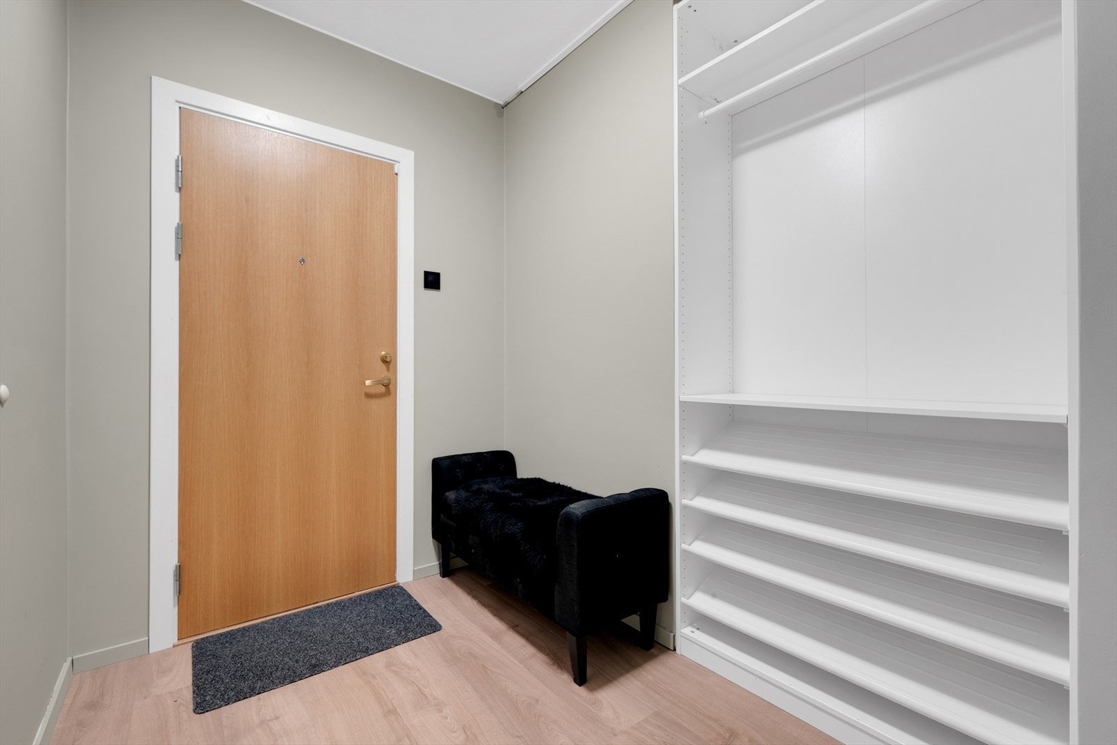 Romslig entré med laminat på gulv, malte slette vegger og malt tak. Det er montert et garderobeskap. Inngang til en romslig og praktisk bod. Galleribilde