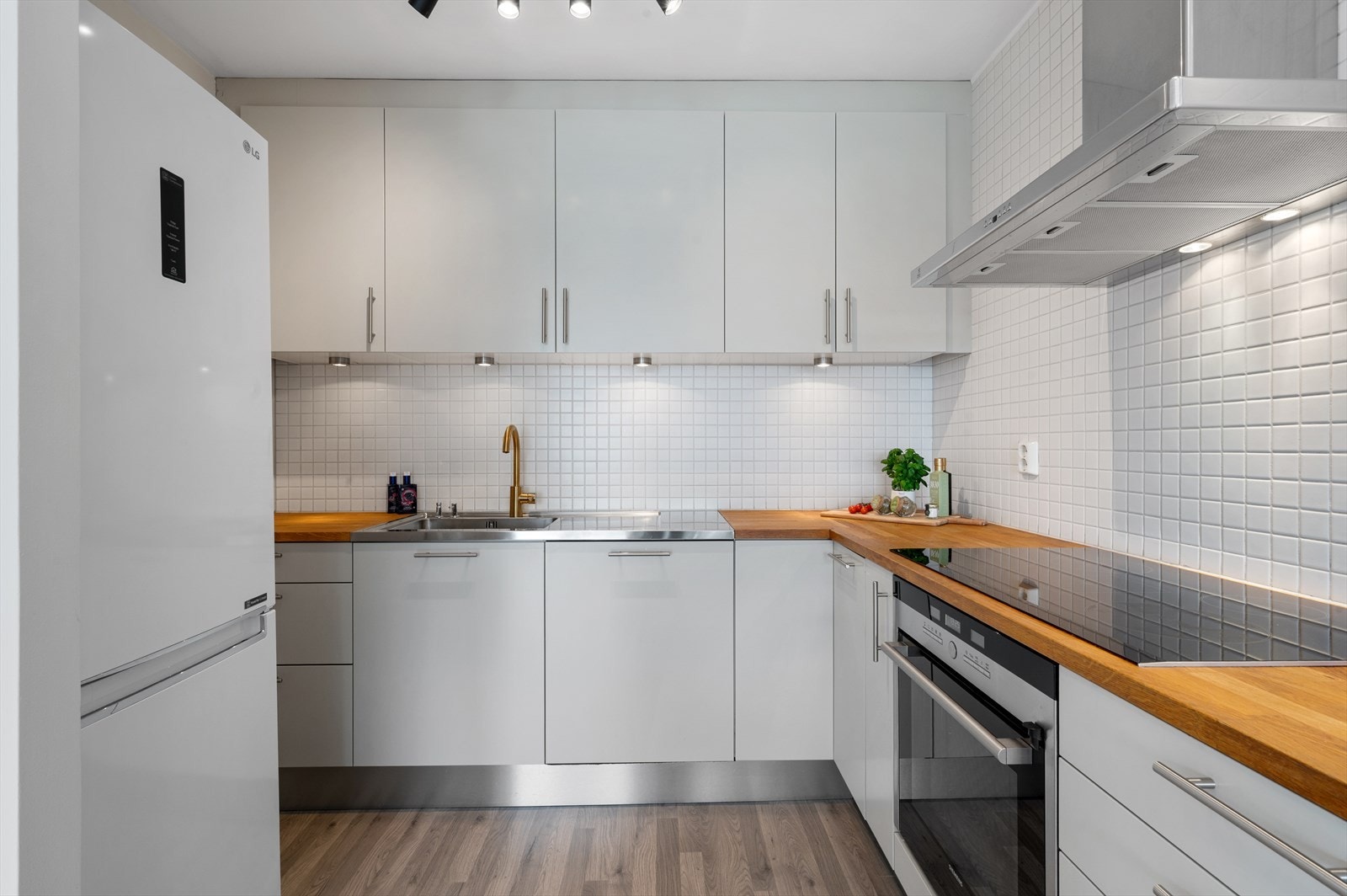 Stilrent Norema-kjøkken med glatte, hvite fronter, benkeplate i heltre og kjøkkenvask i rustfritt stål. Galleribilde