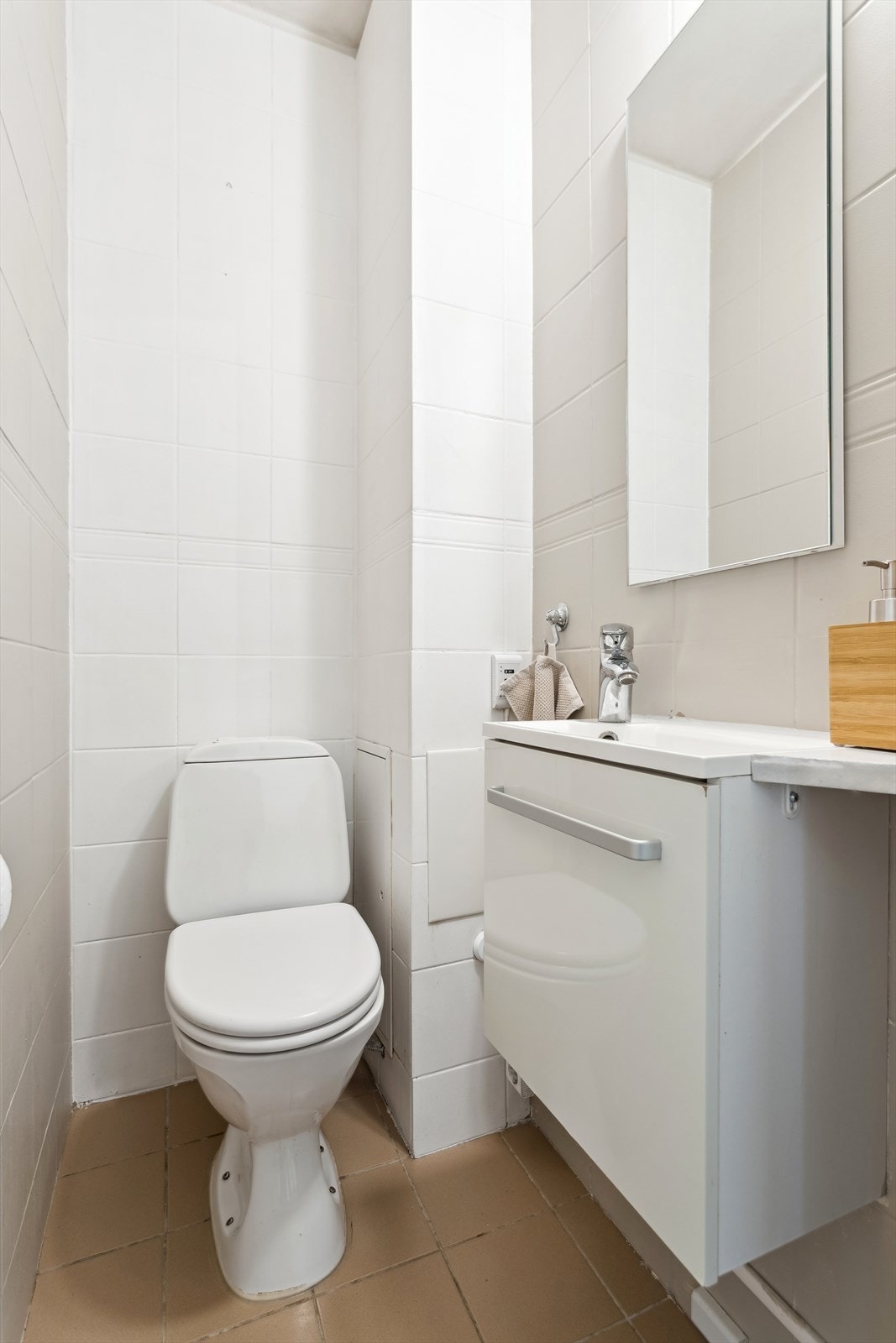 Praktisk toalettrom med flislagt gulv, toalett og enkel vask Galleribilde