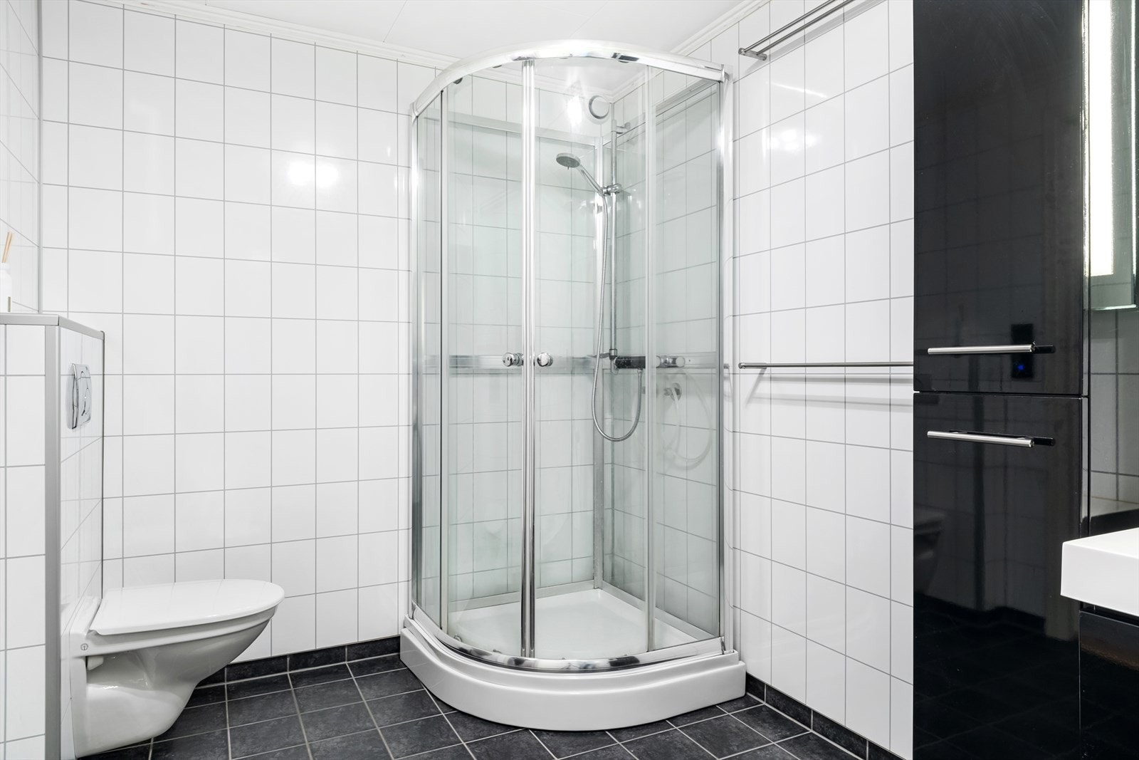 Badet er innreia med vegghengt toalett, dusjkabinett og baderomsmøbel med heildekkande servant og sideskåp. Galleribilde