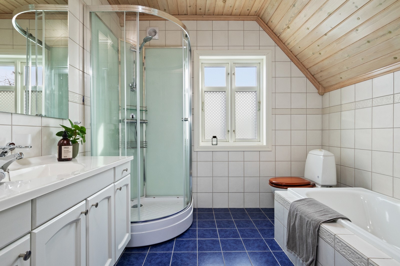 Badet oppe er innredet med hvite veggfliser og mørkeblå gulvfliser for en fin kontrast. Galleribilde