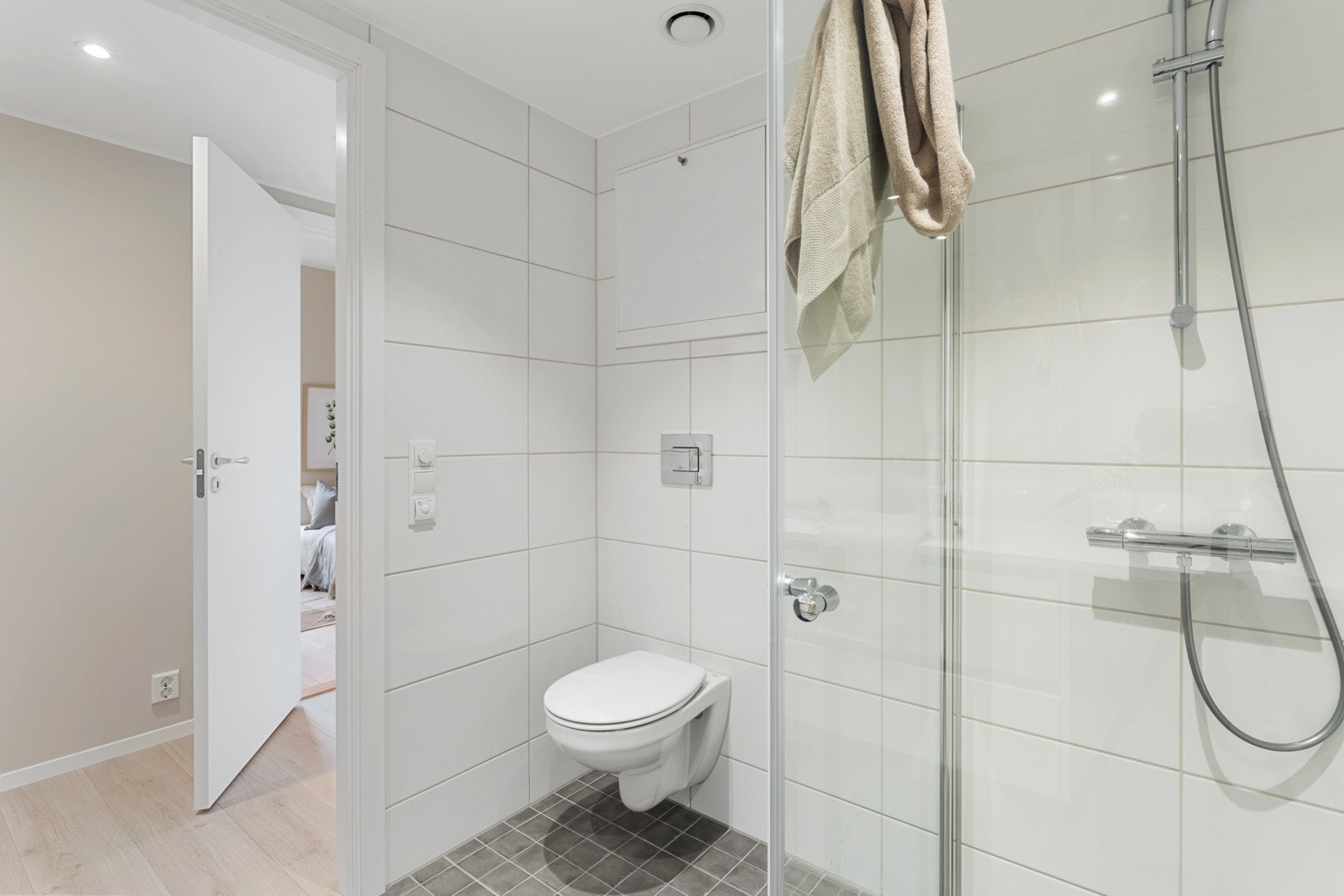 Badet er helfliset med enkle, men tidløse farger. Badet er komplett med vegghengt toalett, dusj, servant med oppbevaring og opplegg til vaskemaskin og tørketrommel. Galleribilde