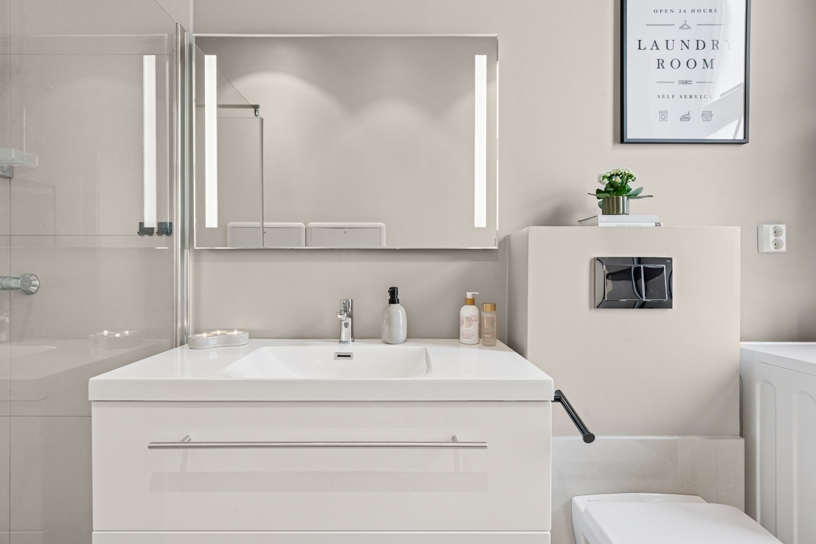 Delikat bad innredet med dusj, vegghengt toalett og servant med speil og belsyning. Opplegg for vaskemaskin. Galleribilde