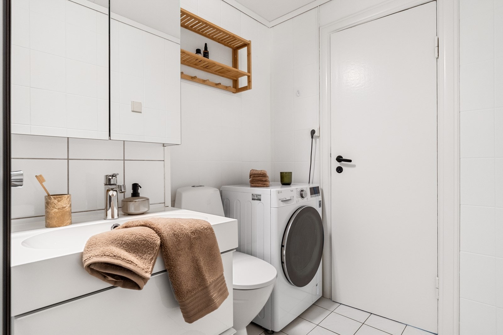 Badet er innredet med dusjdører, servant, toalett, møbler og opplegg for vaskemaskin. Galleribilde