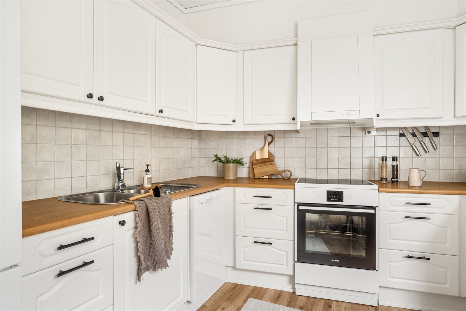 Kjøkkenet er innredet med hvite profilerte fronter, og lyse fliser over kjøkkenbenk. Galleribilde