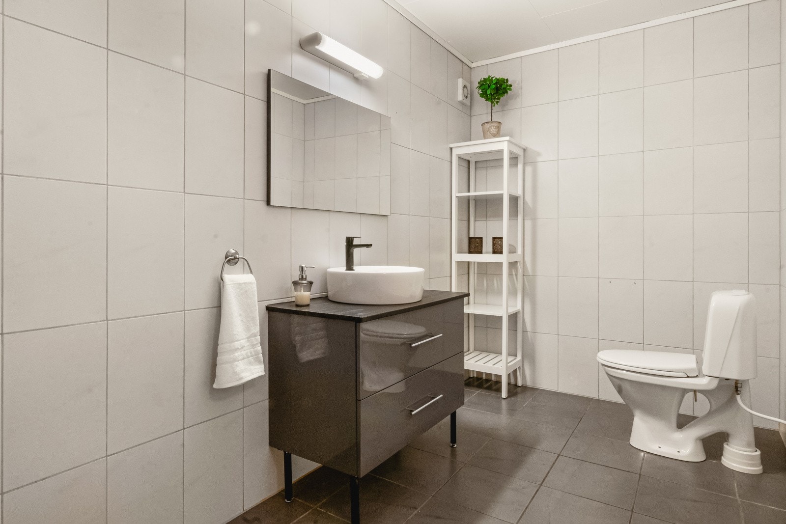 Badet er av god størrelse og er innredet med baderomsmøbel med slette fronter og benkeplate i heltre, samt speil og gulvstående toalett Galleribilde