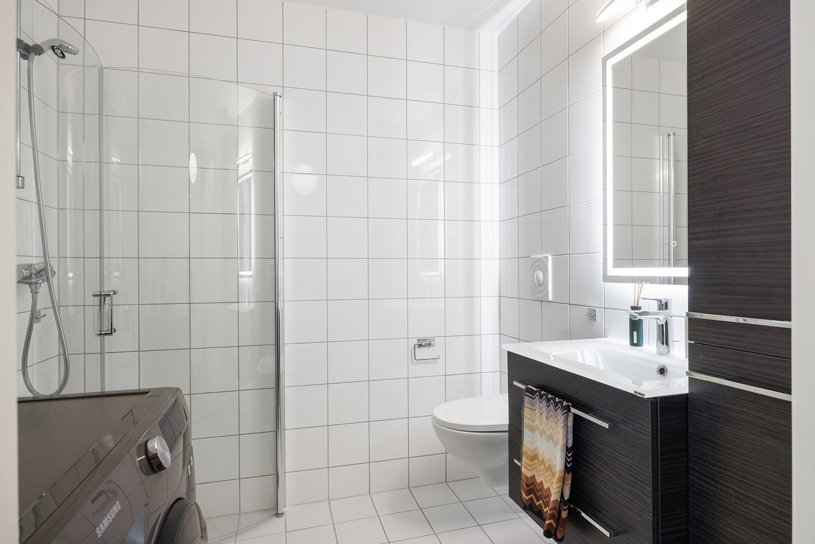 Badet har veggmontert WC, dusjplass med innadslående dusjvegger og servant med ettgreps blandebatteri i innredning. Galleribilde