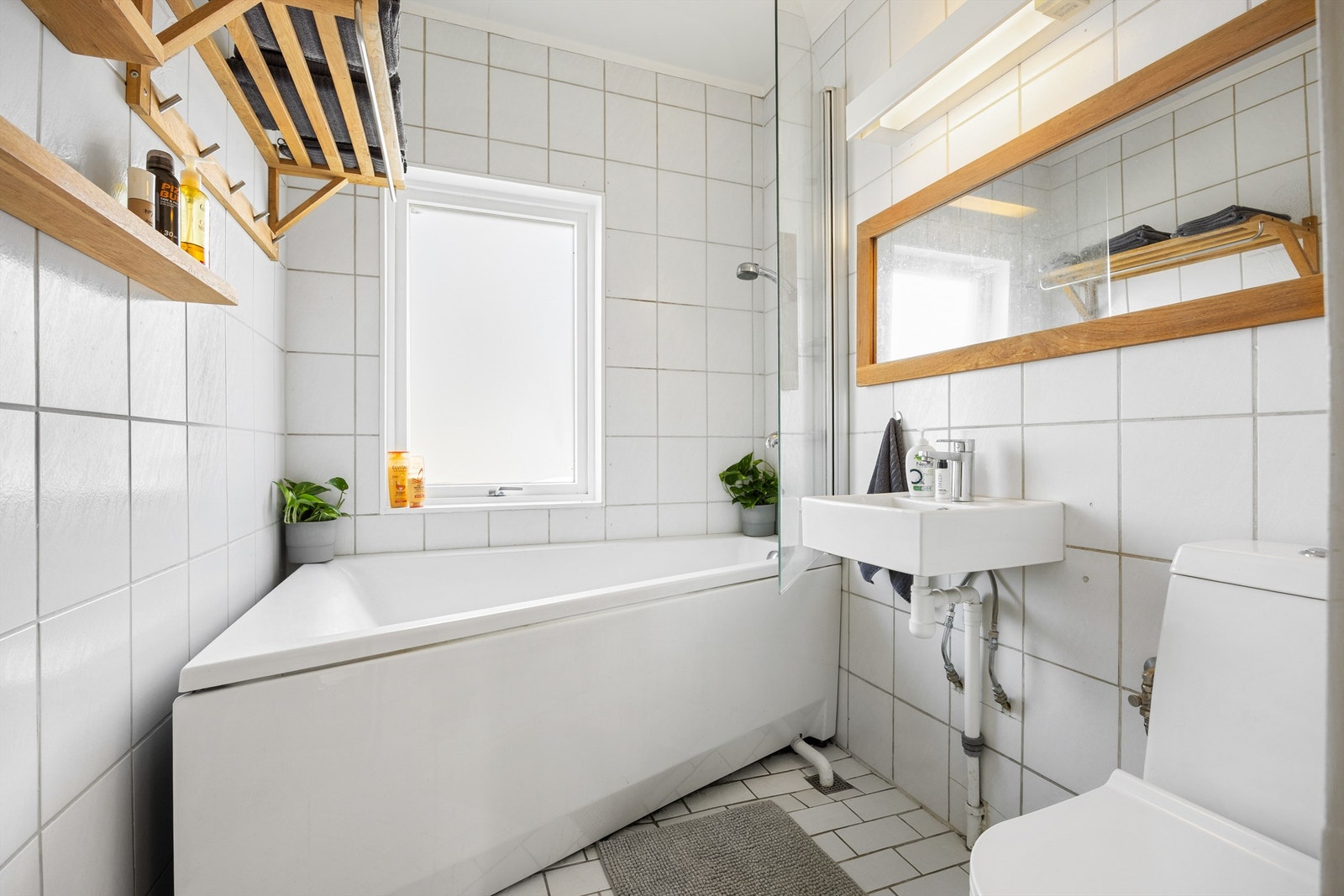 Lyst flislagt bad med dusjing i badekar og frittstående toalett Galleribilde