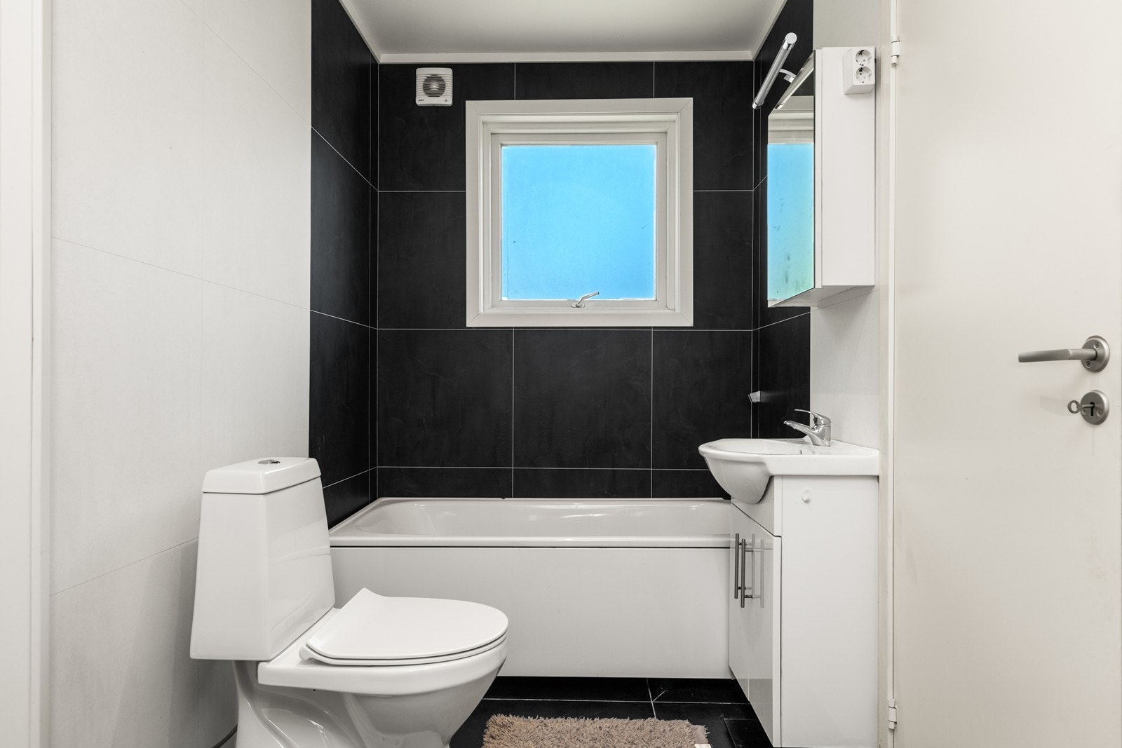 Baderommet i 1. etasje har fliser på gulv og vegger, og er utstyrt med heldekkende servant i innredning med speilskap over. Videre er det gulvmontert wc og badekar Galleribilde