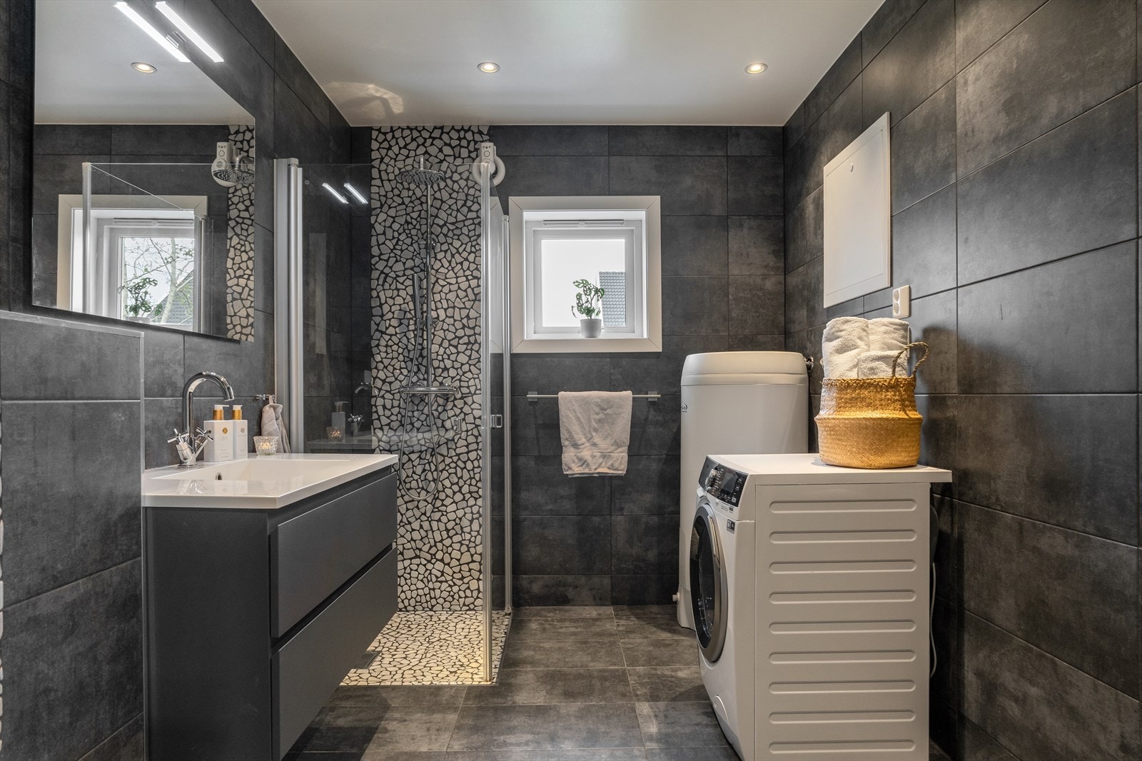 Tiltalende fliselagt baderom med baderomsseksjon, dusj, vegghengt wc og opplegg for vaskemaskin Galleribilde