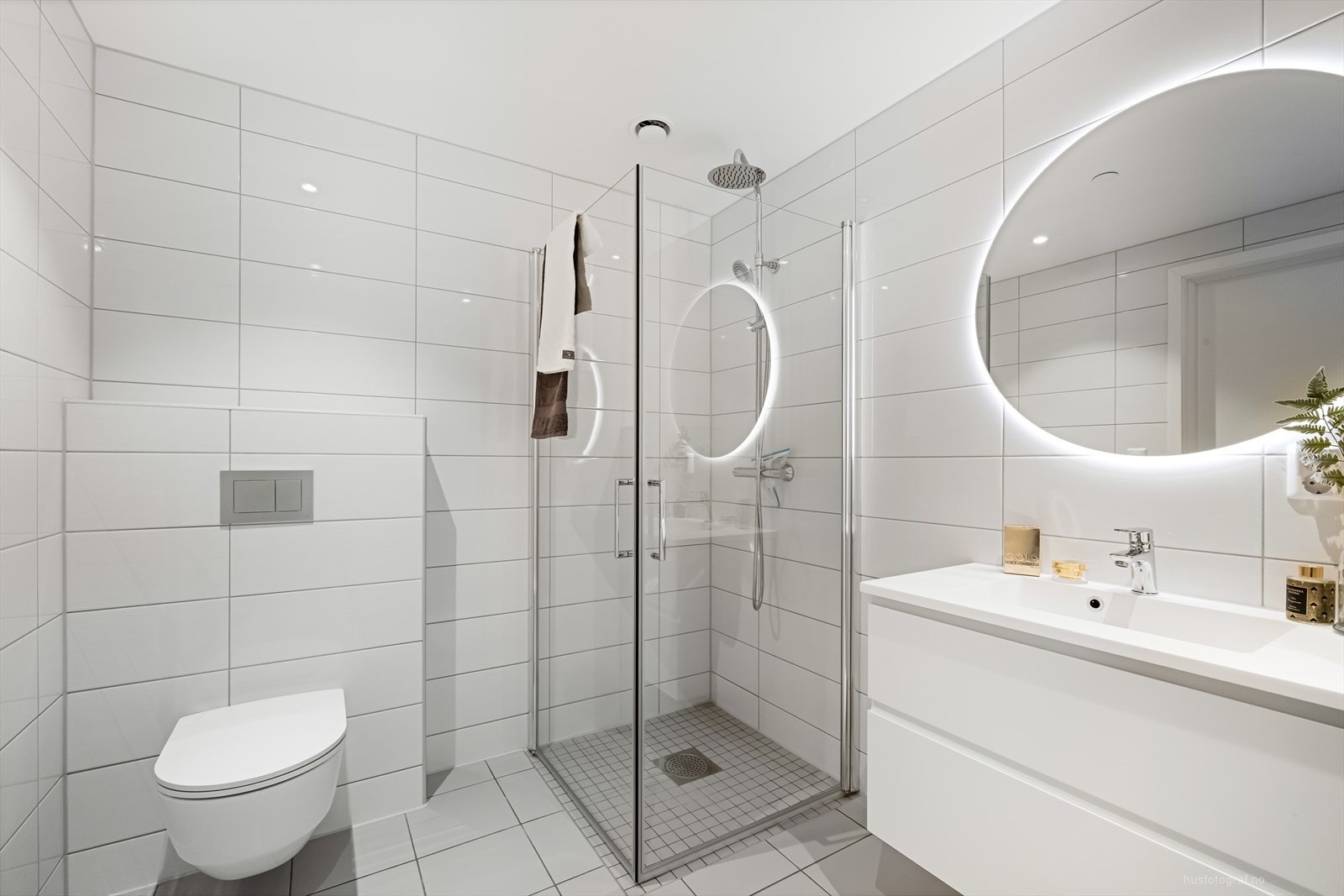 Badet er innredet med heldekkende nedfelt servant med rom for oppbevaring i skuffeseksjon, speil med led lys, vegghengt toalett og dusjhjørne med innfellbare dusjvegger. Galleribilde