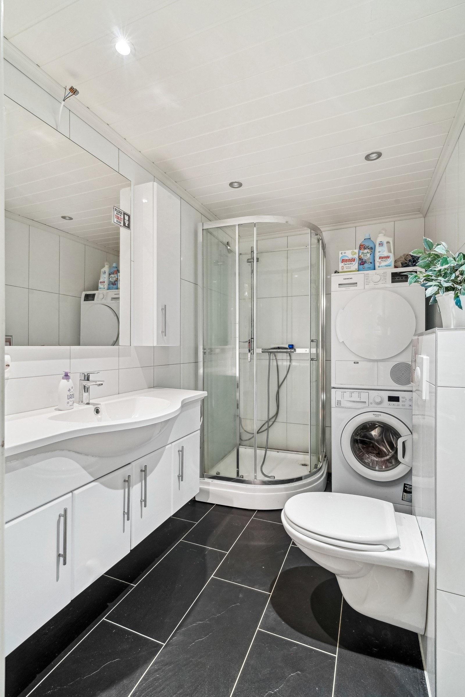 Helfliset bad/vaskerom med gulvvarme, og ledspotter i himling. Innredet med dusjkabinett, vegghengt toalett, servantinnredning, opplegg for vaskemaskin og tørketrommel. Galleribilde