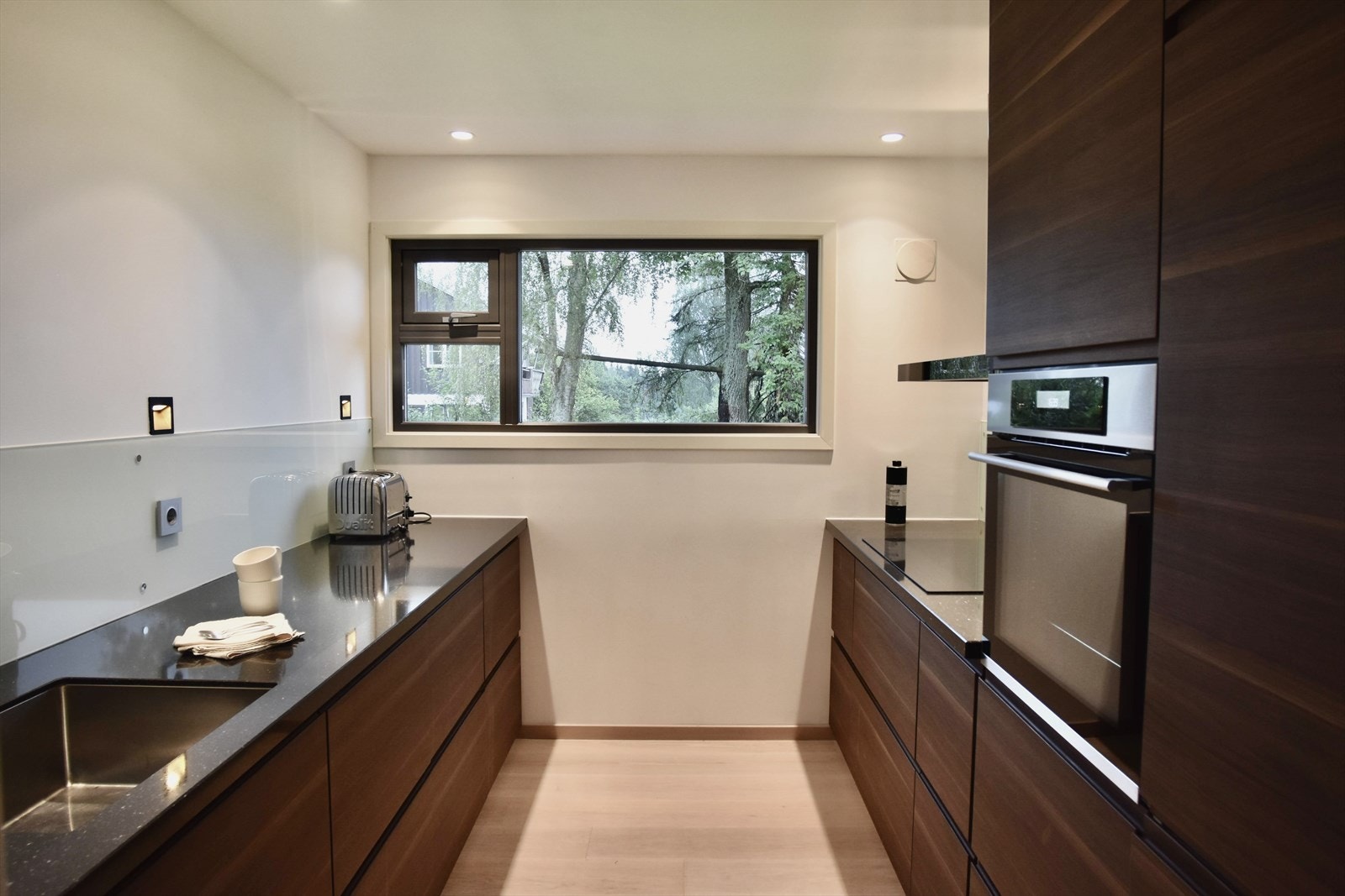 Nyere kjøkkeninnredning med kompositt benkeplate, underlimt vask, integrerte hvitevarer og avtrekk fra koketopp til friluft. Galleribilde