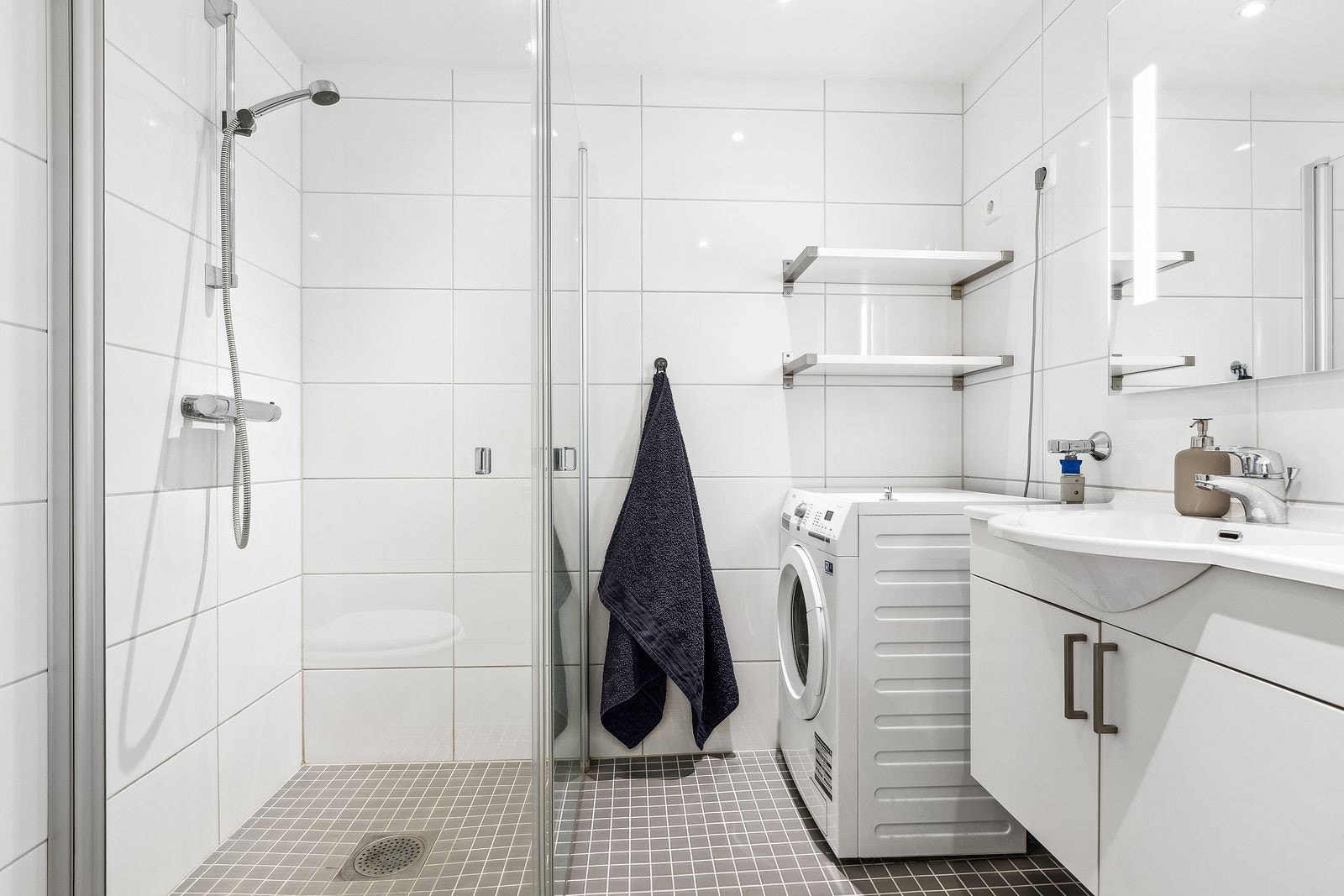 Pent flislagt bad med dusjhjørne i glass og opplegg for vaskemaskin. Galleribilde