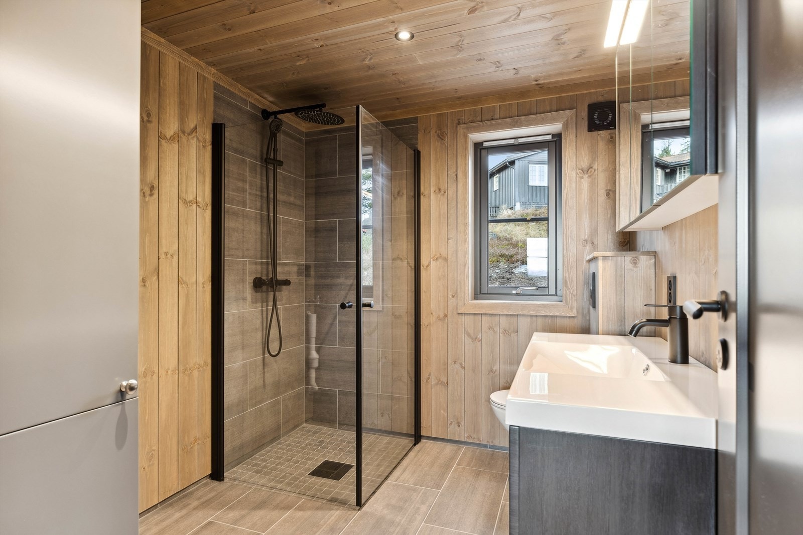 I tillegg har hytta et romslig bad/vaskerom innredet med baderomsinnredning (100 cm) med heldekkende servant, speilskap med lys over, dusjnisje 90x90 cm, veggmontert toalett. Det er skap for bereder og opplegg for vaskemaskin. Galleribilde