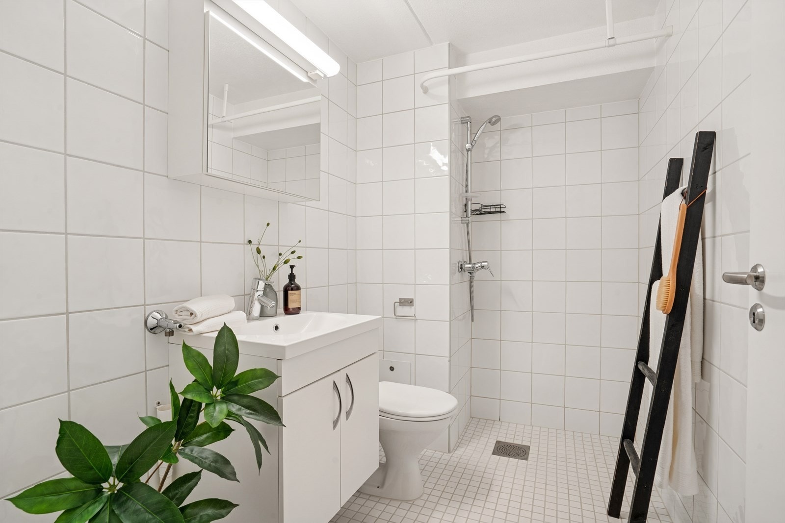 Leilighetens baderom har fliser på gulv og vegger, og varmekabler i gulvet. Baderommet er innredet med servantinnredning, speilskap, dusj og toalett. Galleribilde