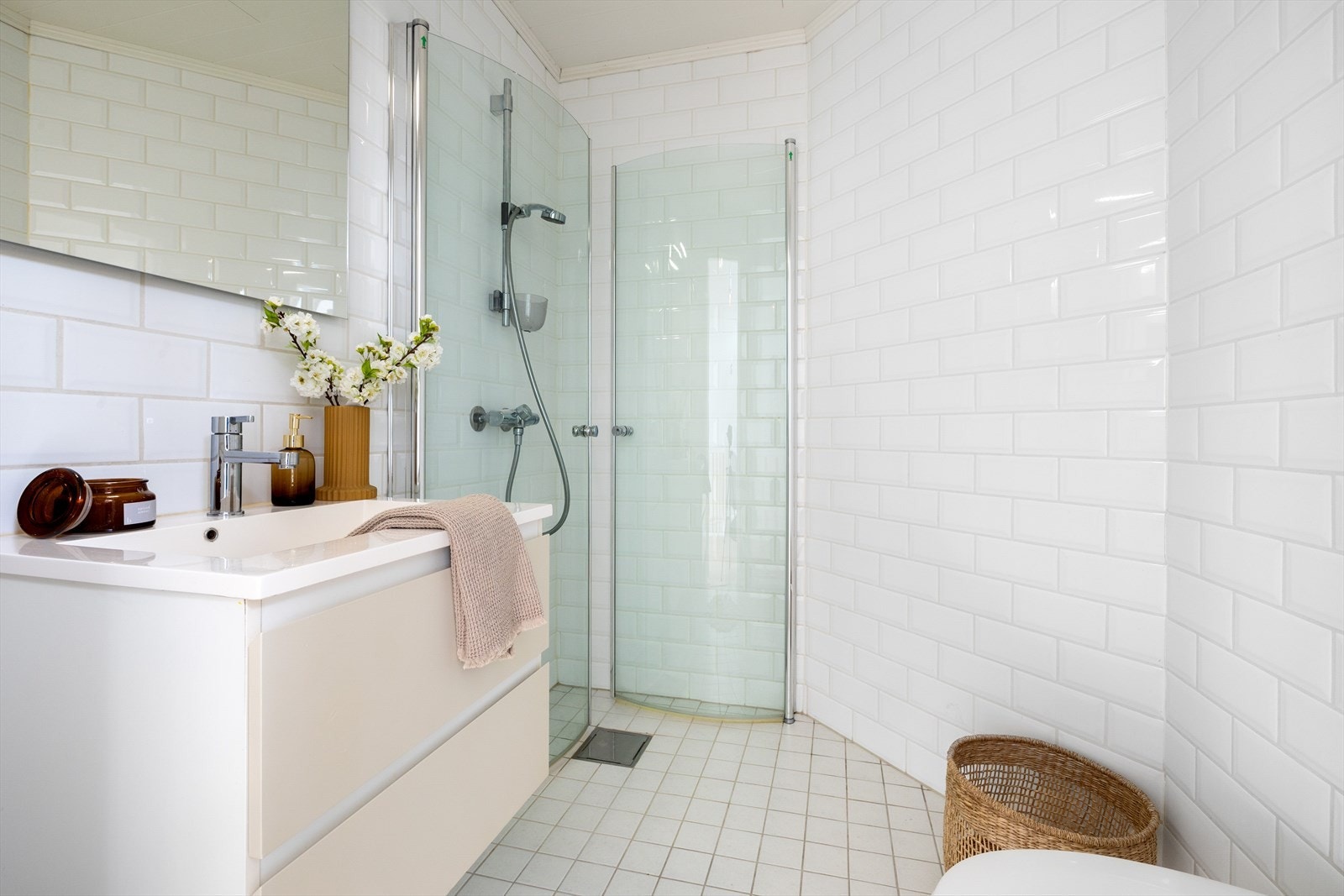 Baderom med tilkomst fra hall med fliser på gulv og vegger. Badet har vegghengt toalett, dusjhjørne med glassfoldedører og innredning med skuffeseksjon og speil. Galleribilde