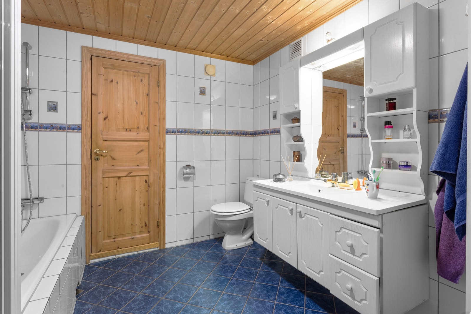 Badet er utstyrt med dusjnisje med skyvedør, gulvmontert klosett, innebygd badekar og servantskap med profilerte fronter og heldekkende servant. Galleribilde