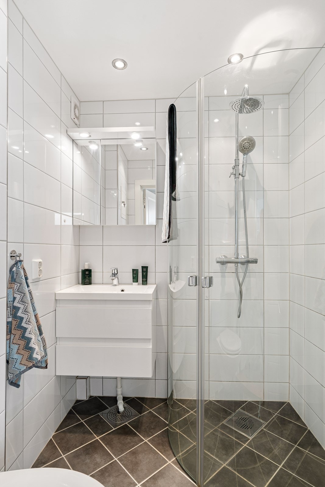 Pent flislagt baderom med regnfallsdusj, helservant på moderne skuffeinnredning og innfellbare dusjvegger i herdet glass. Galleribilde