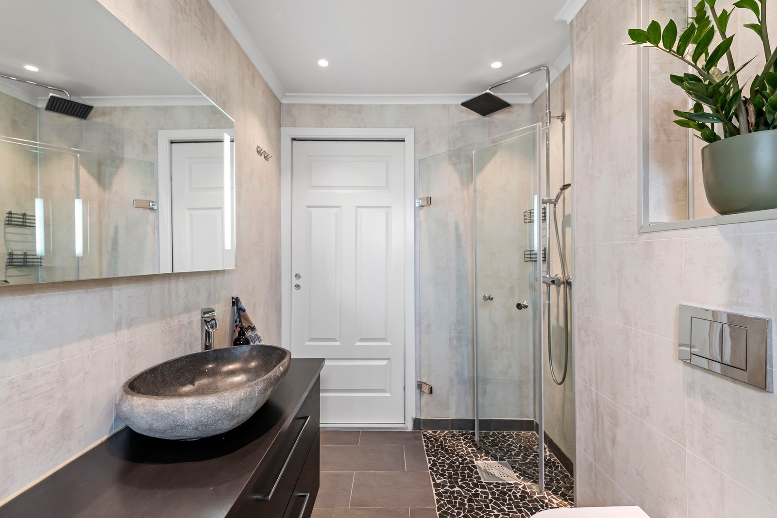 Videre har badet et vegghengt toalett, et ovalt badekar og et dusjhjørne. Dusjhjørnet har fine fliser på gulvet, innfellbare glassdører og en stor regnfallsdusj. Galleribilde