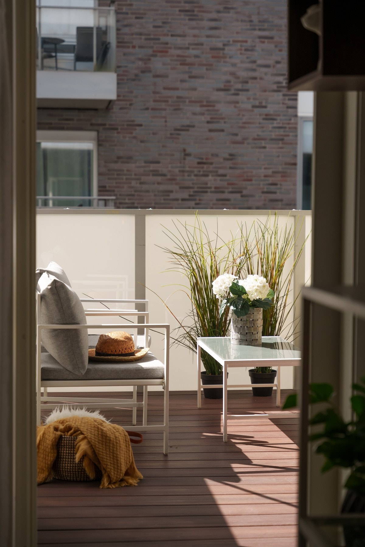 Utgang fra stue til overbygget balkong utstyrt med utelys og stikkontakter. Rekkverk av glass og metall. Gulvoverflate av terrassebord. Galleribilde