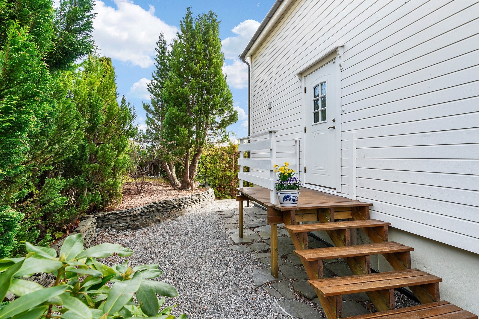 Inngangsparti med tretrapp på nordsiden og beplantning som skjermer mot vegen. Galleribilde