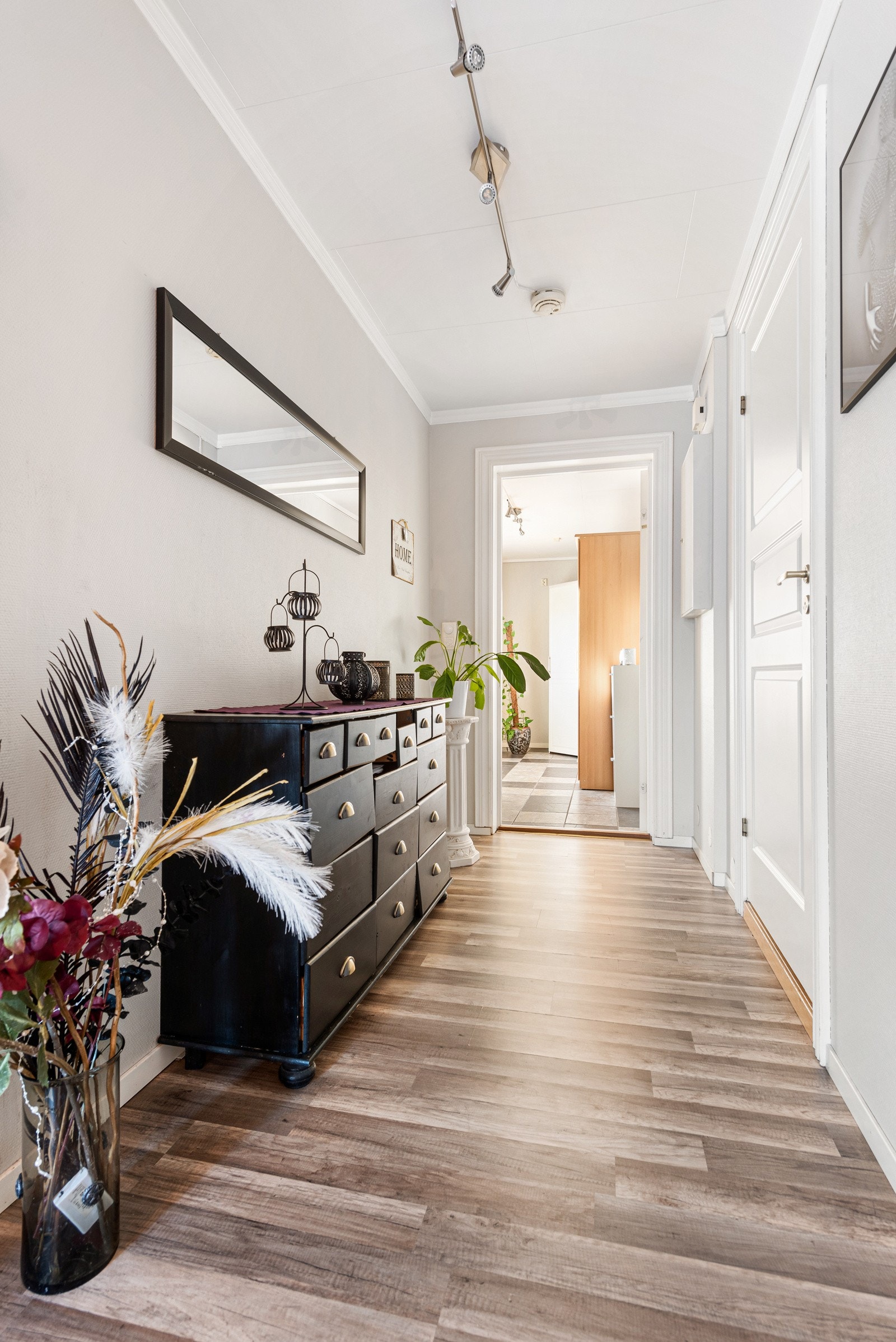 Fra entreen er det glassdør inn til en gang med åpen løsning mot stuen og plass til mer entrémøblement. Gangen har gråmalte vegger og nøttefarget laminatgulv, samt adkomst til to soverom og bad. Galleribilde