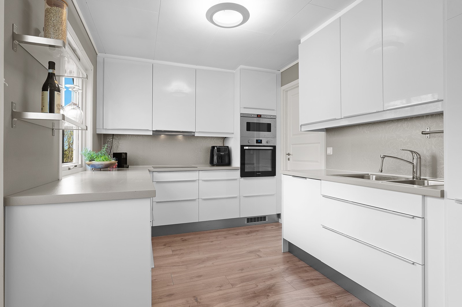 Innredning i hvit høyglans med laminert benkplate, integrerte hvitevarer og servant. Galleribilde