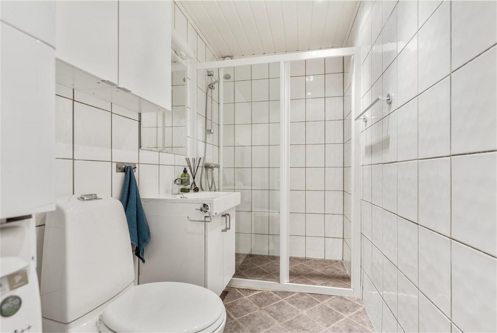 Baderommet er flislagt med varmekabler i gulv - Dusjsone, vegghengt skap, servant med speil montert på vegg, vaksemaskin og tørketrommel Galleribilde