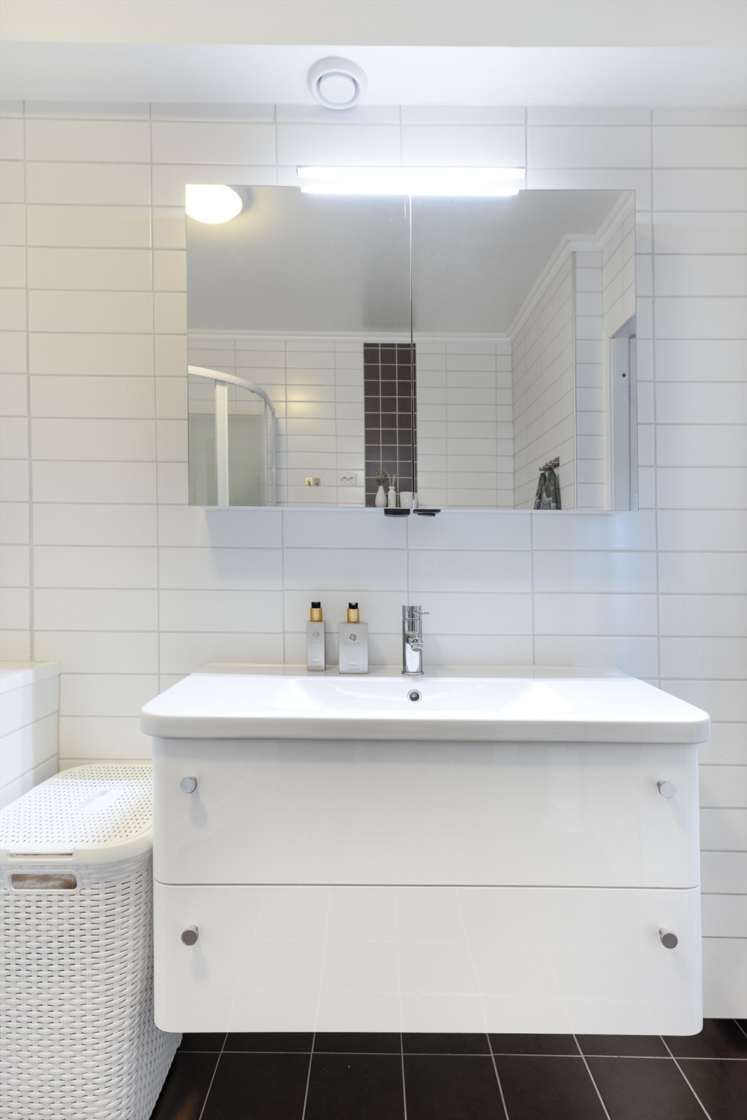 Vegghengt baderomsinnredning med dobbel skuffeseksjon og ovenpåliggende servant. Over innredningen er det vegghengt speilskap som gir ekstra oppbevaringsplass, med overlys og stikkontakt Galleribilde