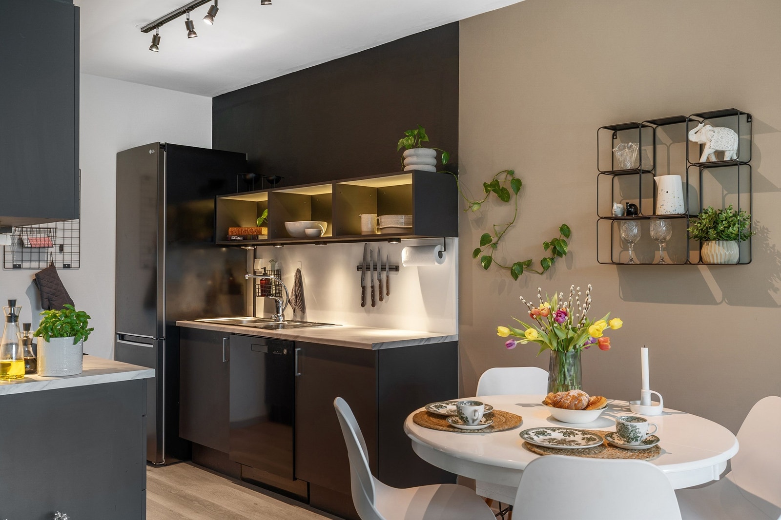 Spisestuen gir et naturlig skille inn mot kjøkkenet. Godt utnyttet kjøkkeninnredning med oppbevaringsmulighet i både over- og underskap. Legg merke til lysdetaljene som er montert i den åpne vegghyllen! Galleribilde