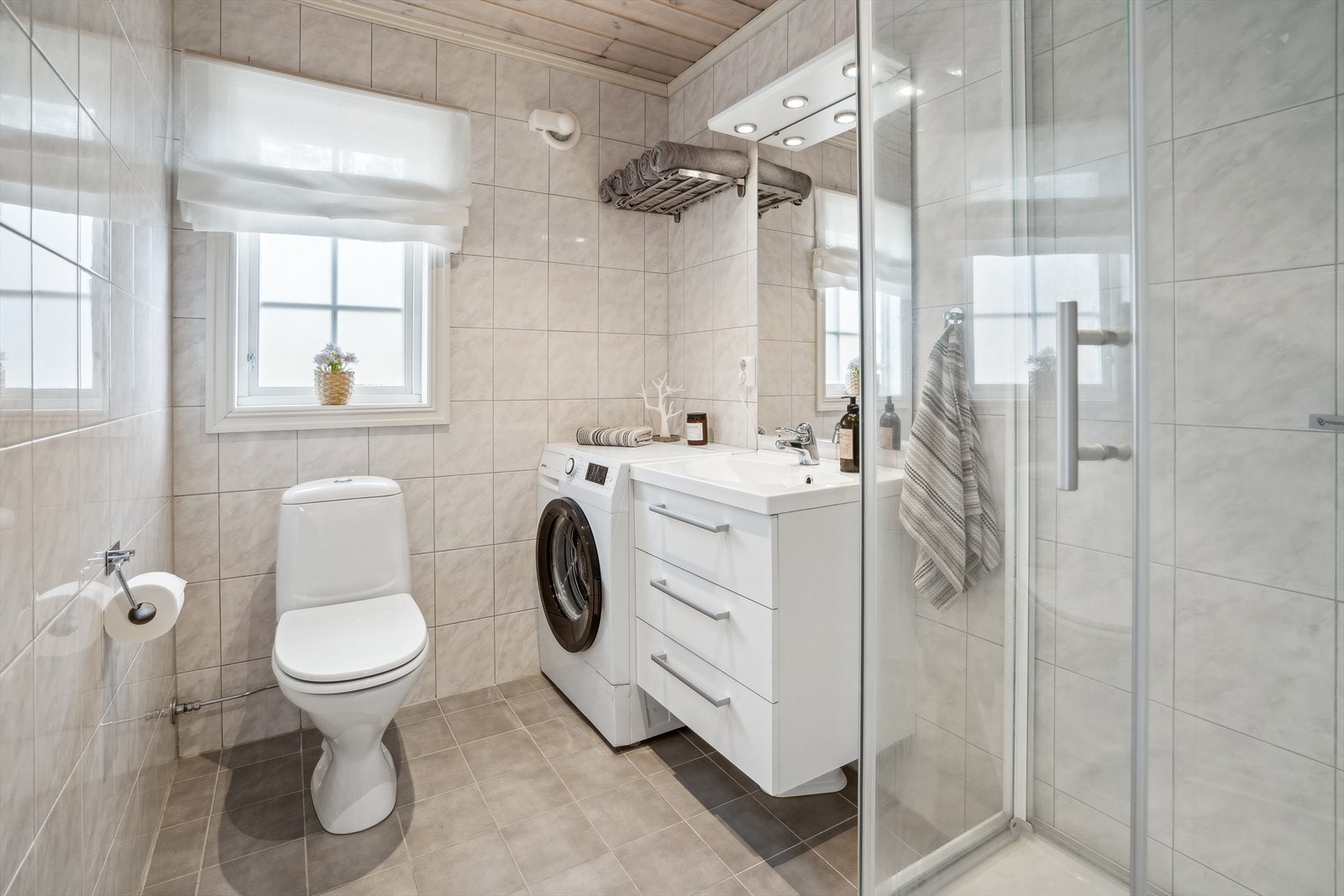 Delikat, flislagt baderom. Rommet inneholder innredning med nedfelt servant, toalett, dusjkabinett og opplegg for vaskemaskin. Galleribilde