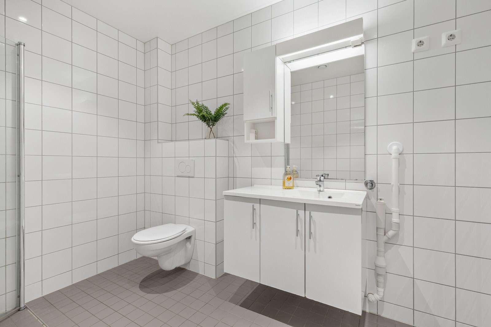 Badet inneholder WC, dusjhjørne, servantinnredning med speil, samt opplegg til vaskemaskin. Galleribilde
