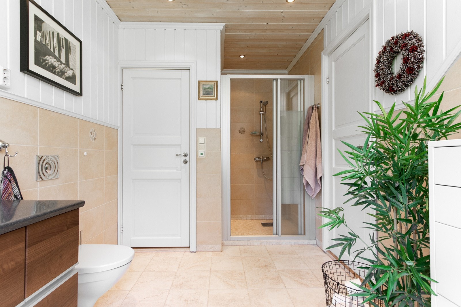 Badet har ekstra takhøyde med downlights og varmekabler på gulv. Det er toalett, dusjhjørne med skyvedører, servant med skuffer og speil med lampetter. Galleribilde