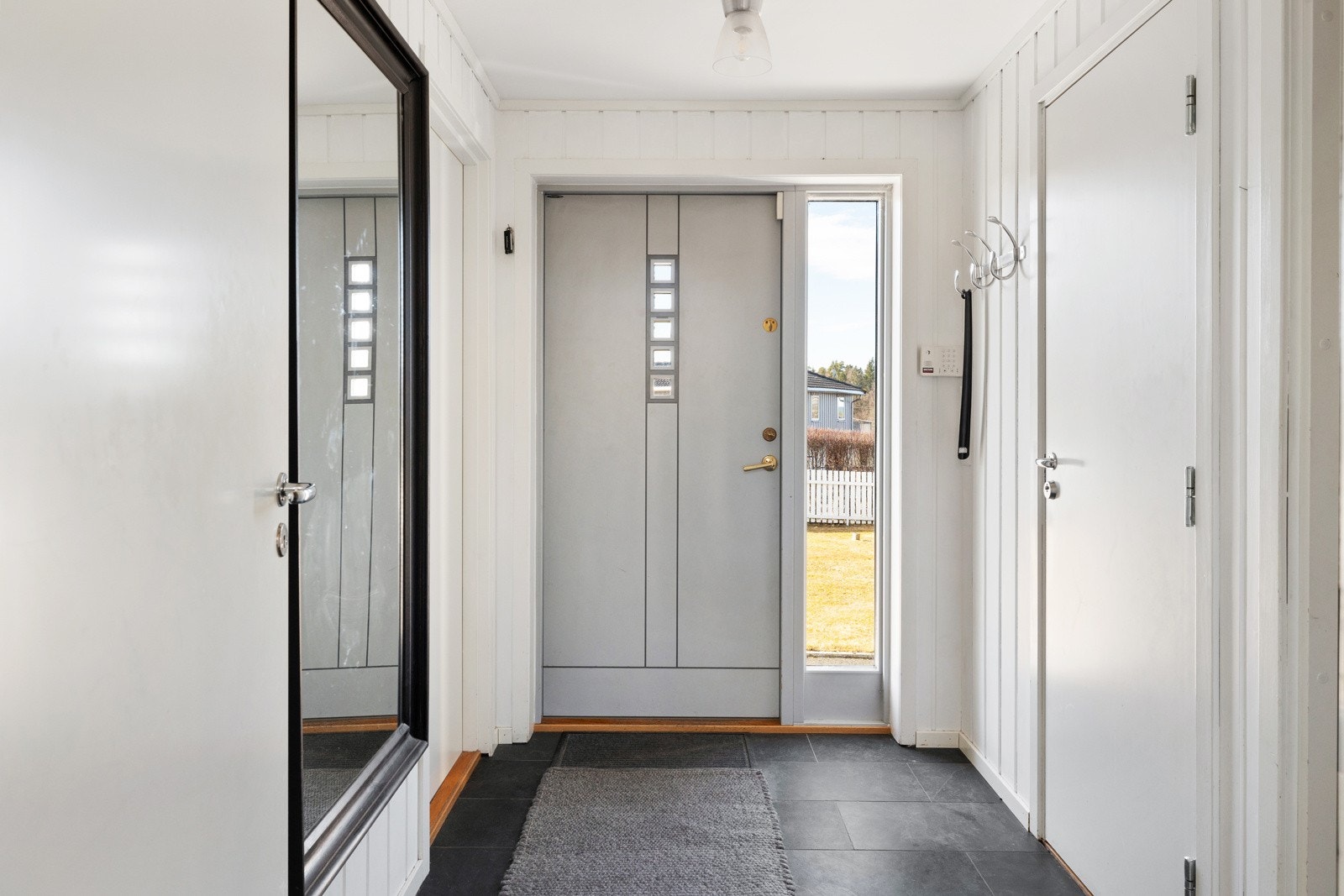 Velkommen inn! Entréen er lys og innbydende, med lyse vegge, gulvet er lagt med mørke fliser som gir en fin kontrast. I gangen henger en knaggrekke der du enkelt kan henge fra deg jakker og yttertøy. Galleribilde