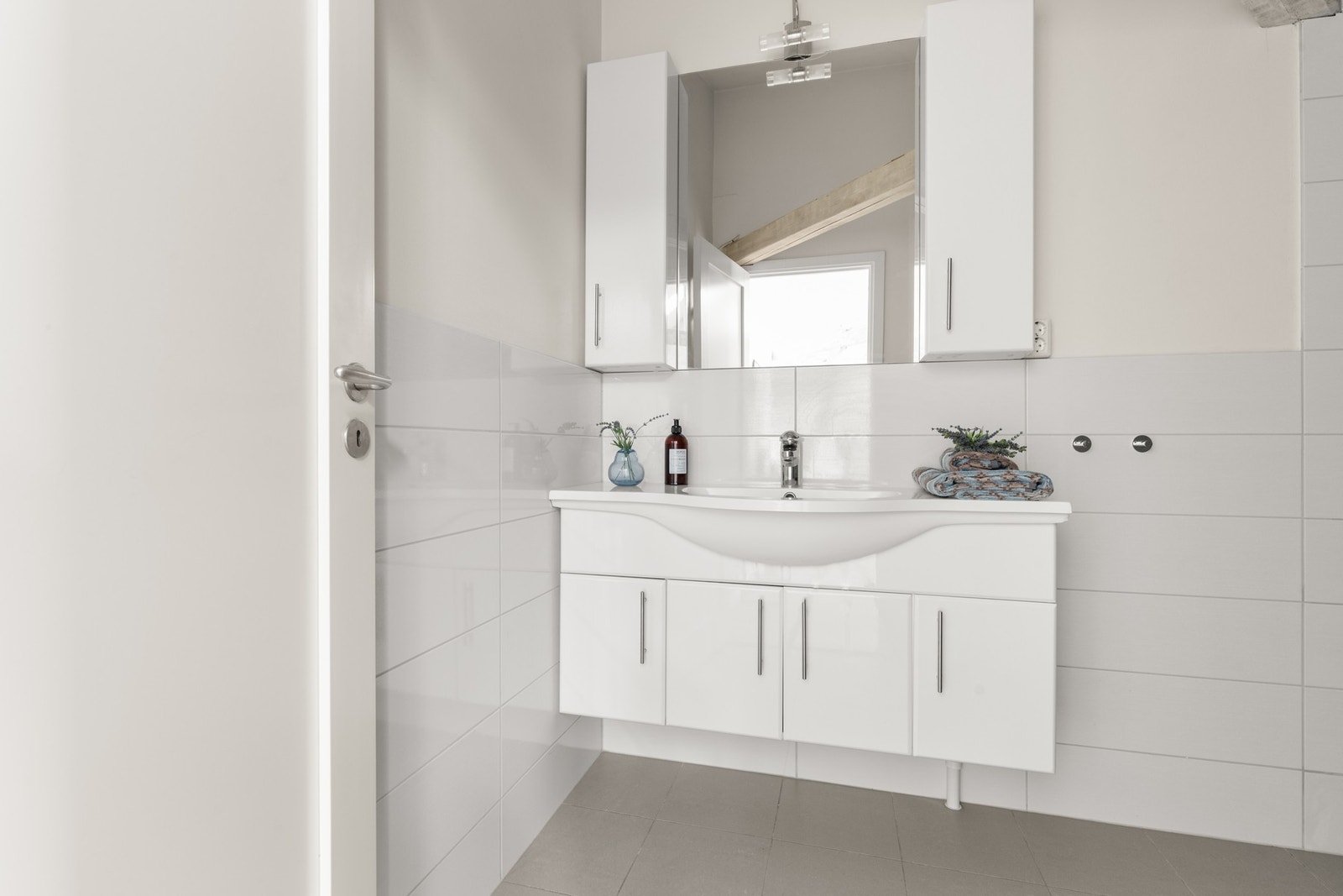 Badet er utstyrt med dusj med innfellbare glassvegger, servantseksjon med skap og heldekkende komposittvask, overskap, speil med lys og gulvmontert wc. Galleribilde